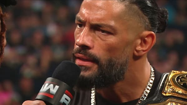 Roman Reigns speaks into a WWE microphone during a tense promo on Raw, with his championship belt visible on his shoulder.