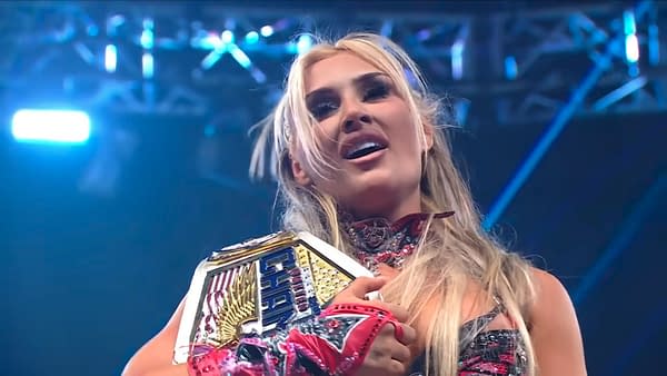 Tiffany Stratton smiles and clutches the United States Championship after winning it on WWE SmackDown. Blue arena lights glow behind her.