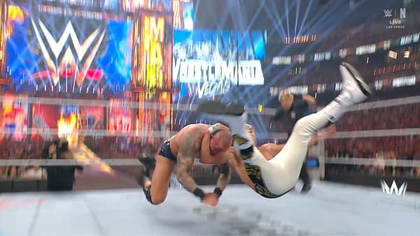 A wrestling match scene at WrestleMania, featuring a dramatic move where one wrestler is executing an RKO on another. The background is filled with colorful lights and a WWE logo.
