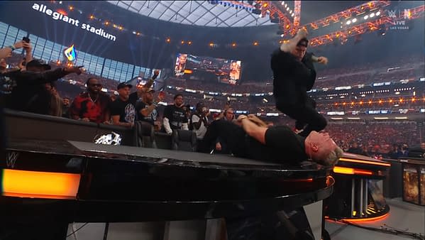 A wrestler leaps from a standing position to perform a move on another wrestler lying on a table, while a crowd watches in excitement at Allegiant Stadium during WrestleMania.