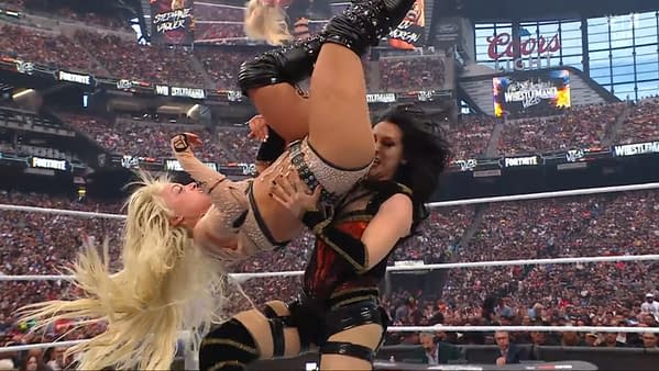 A female wrestler is performing a powerful move, lifting another wrestler upside down. The setting is a packed arena, with fans cheering in the background.