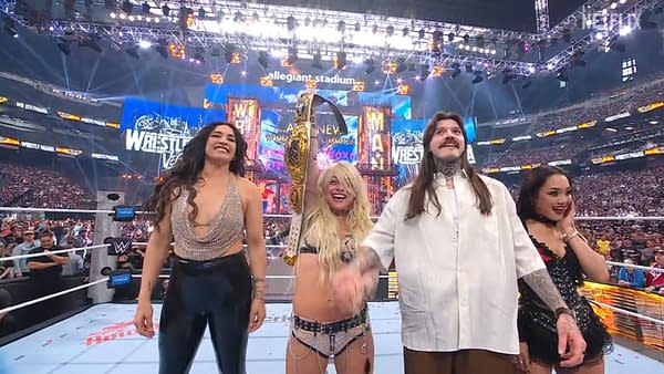 A group of four celebratory individuals stands in a wrestling ring after a championship match, with one person holding a championship belt high. The arena is filled with cheering fans and vibrant lights, creating an electric atmosphere.