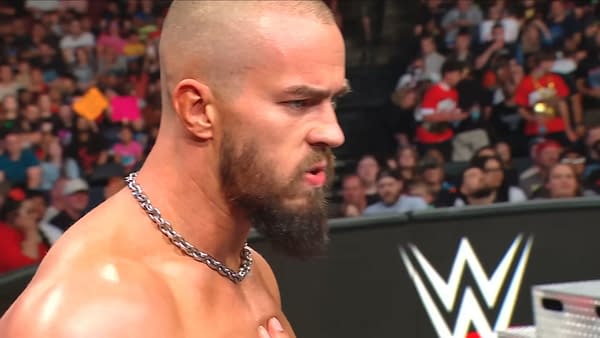 Austin Theory glares intensely in the WWE Raw ring, looking furious as the crowd watches in the background.