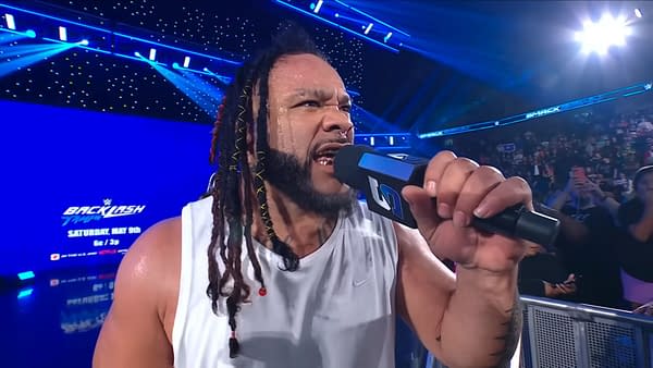 Jacob Fatu shouts into a WWE microphone on SmackDown, with the arena lights blazing behind him.