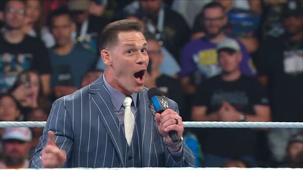 John Cena stands in the WWE ring in a striped suit, speaking excitedly into a microphone during a Backlash announcement. He appears to be unveiling the John Cena Classic.