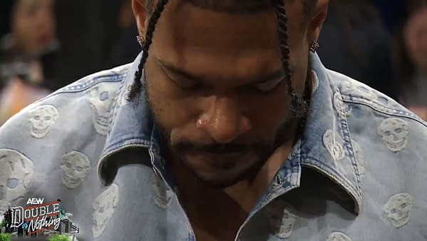 Kevin Knight looks down with a frustrated expression during AEW Double or Nothing, wearing a light denim shirt with skull patterns.