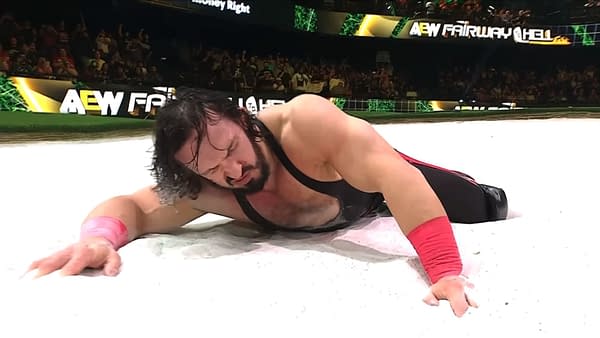 PAC lies face down in a sand trap during AEW Collision: Fairway to Hell, reaching forward as the crowd watches from the arena seats.