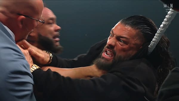 Jacob Fatu chokes Roman Reigns against the ring ropes during a brutal WWE Raw attack, with Paul Heyman nearby. Reigns grimaces in pain as Fatu squeezes his neck.