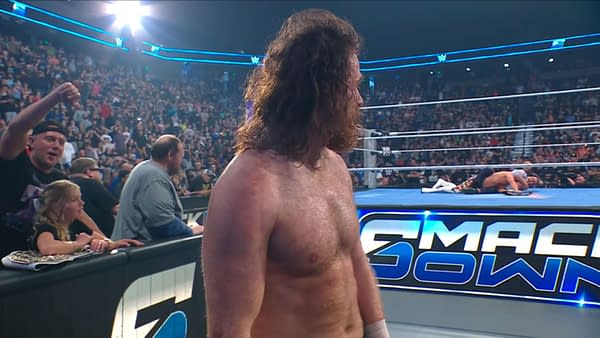 Sami Zayn stands at ringside during WWE SmackDown, looking away from Cody Rhodes after walking out on him. The crowd watches the tense moment unfold.