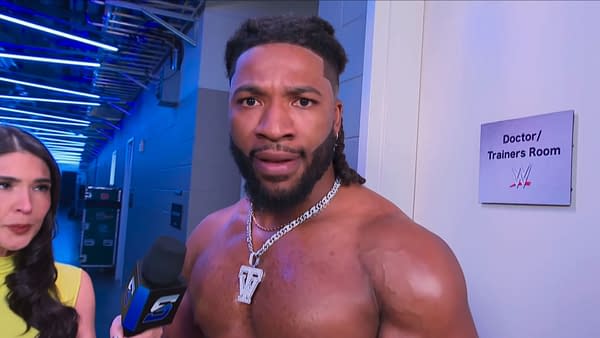 Trick Williams looks stunned during a backstage WWE SmackDown interview outside the doctor/trainers room. A reporter stands beside him as he reacts to news about his Gingerbread Man mascot.