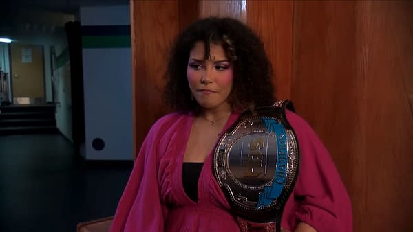 Willow Nightingale stands in a backstage hallway with the TBS Championship over her shoulder, looking serious and emotional.