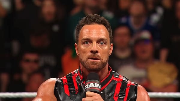 LA Knight stands in the ring on WWE Raw, holding a microphone and looking intensely at the crowd. He wears a black-and-red outfit against a blurred arena audience.
