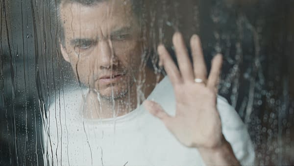 Wagner Moura as Jason in The Last House, seen through rain-streaked glass with his hand pressed against the window.