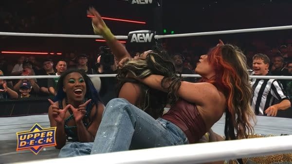 AEW wrestling scene with Maya World on the mat as Mercedes Moné restrains her after a post-match attack, while Athena reacts nearby. The arena crowd watches from ringside.