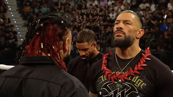 Roman Reigns stands face to face with Jacob Fatu in the WWE Raw ring, both wearing black shirts and intense expressions. The crowd watches behind them as the confrontation unfolds.