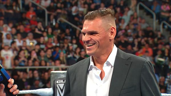 Gunther smiles in a suit inside the WWE ring during SmackDown, appearing amused as the crowd looks on.