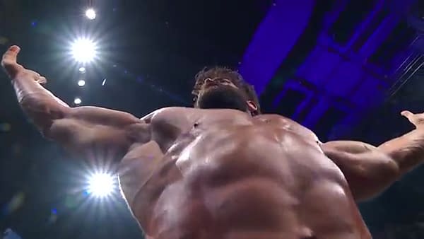 A bottom-up view of the muscular form of Brian Cage as he poses during an AEW Dynamite match with Darby Allin