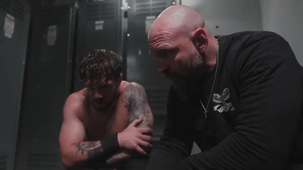 In a dimly lit locker room, Jon Moxley is seen giving advice to Will Ospreay, both mens' faces shrouded in shadow.