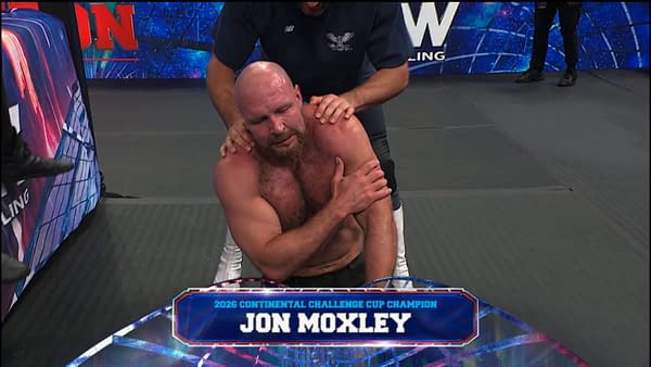 Jon Moxley sits exhausted on the wrestling mat while a staff member steadies him after the match. A graphic identifies him as the 2026 Continental Challenge Cup champion.