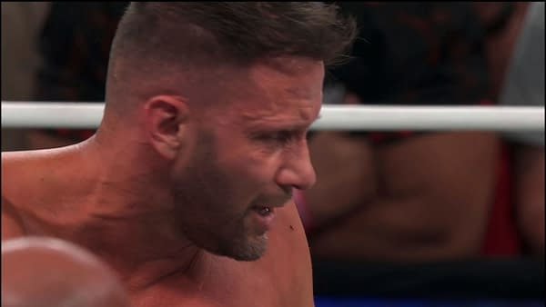 Nigel McGuinness looks down in a wrestling ring, appearing exhausted and disappointed after a match. The AEW All In London moment captures his reflection on the loss.