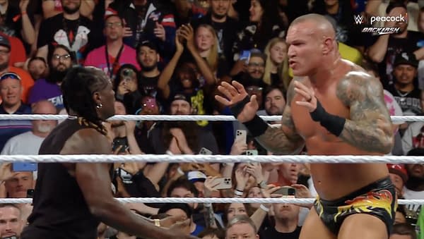R-Truth intervenes as Randy Orton prepares to deliver an RKO to John Cena during a WWE Backlash event, surrounded by an excited crowd.