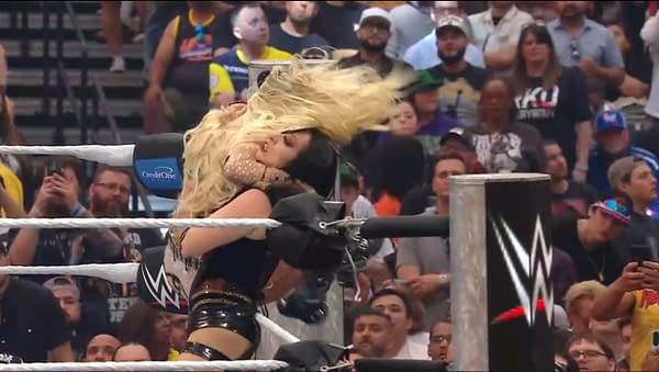 A female wrestler in black attire is delivering a powerful blow to her opponent, who has long blonde hair, in a wrestling ring during a live event. The audience is visible in the background, reacting to the intense match.