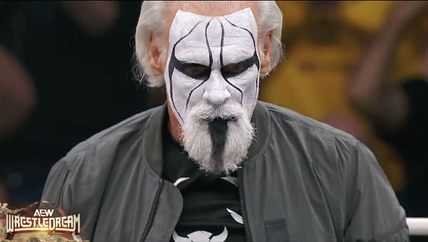 A wrestler known as Sting stands in a ring, wearing dramatic face paint with black and white patterns and a gray jacket. His intense expression captures the energy of the moment.