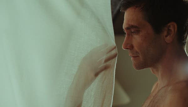 A contemplative close-up of a man in profile standing beside a sheer white curtain, softly lit in warm tones.