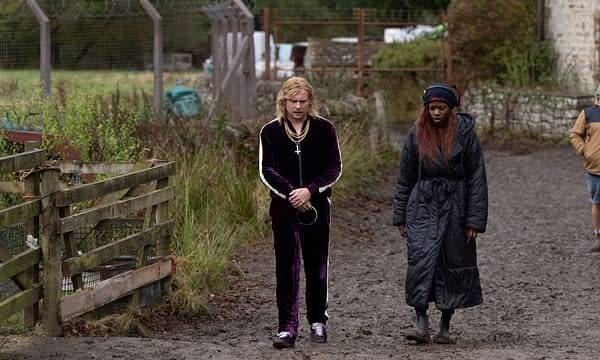 A scene set in a muddy outdoor area, featuring two characters walking together. One is wearing a dark purple velvet tracksuit with a cross necklace, while the other is dressed in a long black coat and boots, both appearing introspective.