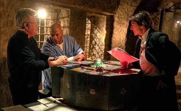 Behind-the-scenes moment from 'Mission: Impossible – The Final Reckoning,' featuring director Christopher McQuarrie, actor Ving Rhames, and Tom Cruise engaged in a scene involving a high-tech device surrounded by tools and documents in a dimly lit setting.