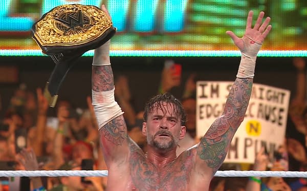 Wrestler CM Punk proudly holds a WWE championship belt above his head in the ring, showcasing his tattoos and intense expression, with cheering fans in the background.