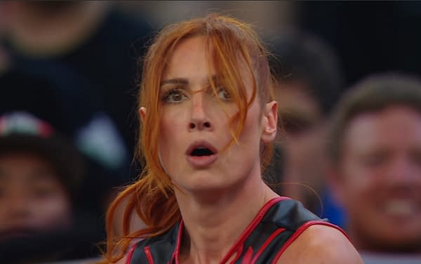A close-up of Becky Lynch with an expression of surprise or determination during a WWE match, wearing a black and red wrestling outfit. The background includes blurred spectators, emphasizing the intensity of the moment.