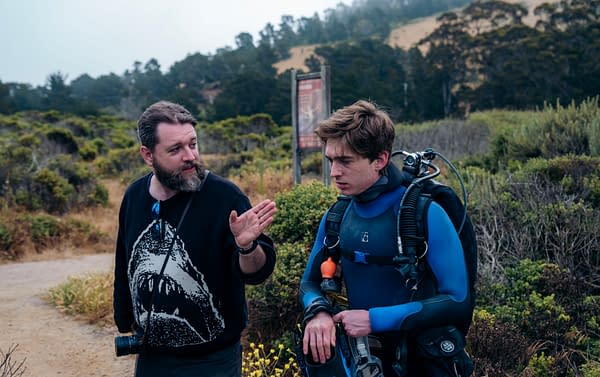 Director Brian Duffield talks with Austin Abrams in scuba gear on the Whalefall set, with coastal hills in the background.