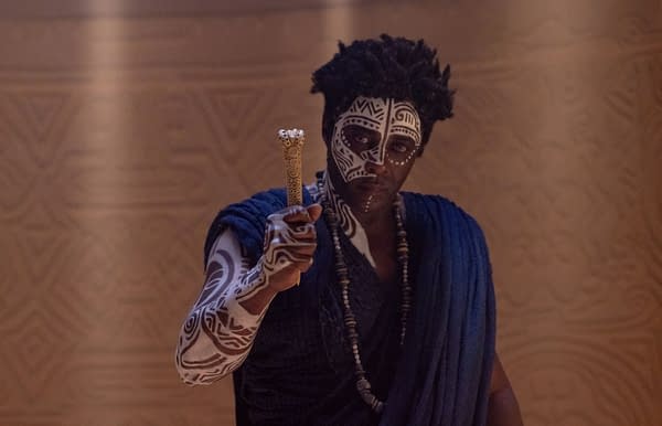 Idris Elba as Lekan in Children of Blood and Bone, holding a carved staff and wearing white tribal face and arm paint.