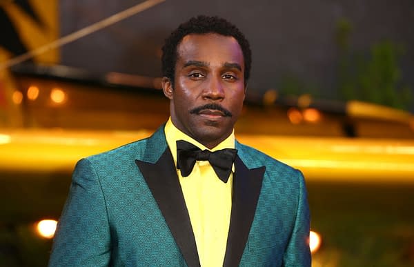 A portrait of actor Tramell Tillman at an event, wearing a stylish teal suit with a black bow tie and a bright yellow shirt, conveying a vibrant and fashionable appearance.