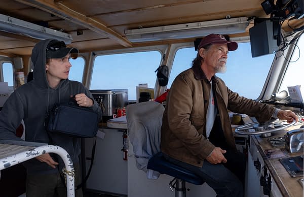 Austin Abrams and Josh Brolin stand in the wheelhouse of a boat in Whalefall, with Brolin steering and Abrams holding a bag.