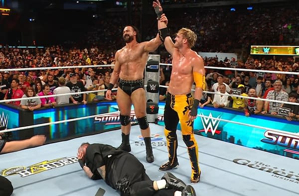 Two wrestlers, Drew McIntyre and Logan Paul, celebrate victory in the ring at WWE SummerSlam, while a defeated opponent, music superstar Jelly Roll, lies on the mat. One wrestler raises the other's arm in triumph, with a cheering crowd in the background.
