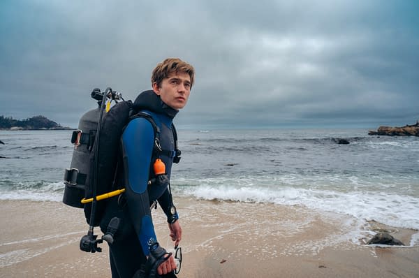 Austin Abrams as Jay Gardiner stands on a beach in a wetsuit and scuba gear, looking out over the ocean in Whalefall.