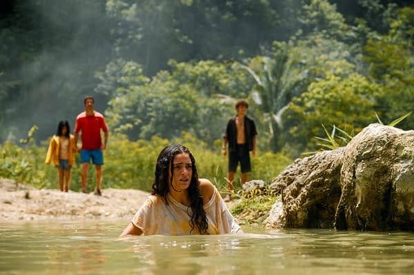 Still from 'Jurassic World Rebirth', featuring Isabella Delgado wading in water, looking concerned, while Reuben Delgado, Teresa Delgado, and Xavier Dobbs stand in the background, surrounded by greenery.