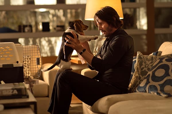 A man sits on a couch, joyfully interacting with a small beagle puppy, who is playfully standing on his lap. The scene is warmly lit, showcasing a cozy living room setting.