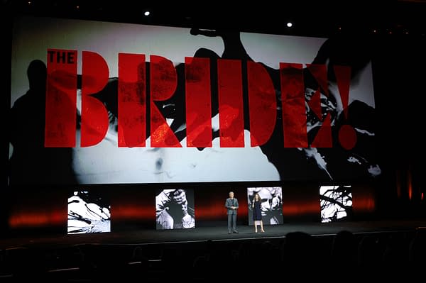 A presentation at CinemaCon showcases the title 'THE BRIDE!' in large, bold red lettering on a screen behind two speakers. The stage is adorned with abstract visuals and silhouettes, creating an engaging atmosphere for the event.