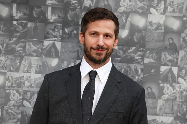 A man with a beard and short hair is smiling, wearing a dark suit and a white shirt with a black polka dot tie. He stands in front of a collage of black-and-white images, suggesting a cinematic theme.