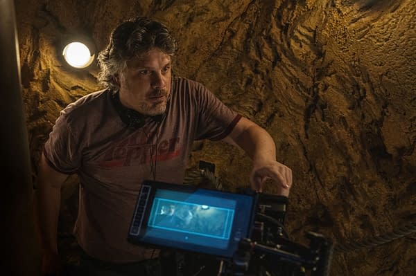 Director Johannes Roberts is seen working on set for the film 'Primate,' surrounded by textured walls and operating a camera monitor.