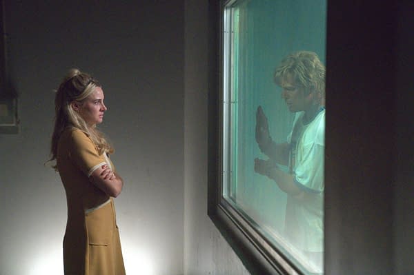 A tense Motor City film still shows a woman standing with arms crossed beside a window, facing another woman's reflection behind the glass.