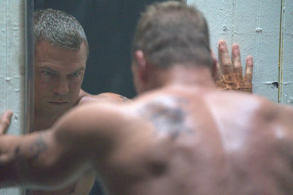 A tense Motor City still shows a shirtless man staring intensely through a narrow opening, with another blurred figure in the foreground.