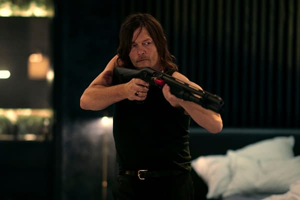 A tense scene featuring a man holding a shotgun, dressed in a sleeveless shirt, with a focused expression. The background hints at a dimly lit interior with soft furnishings.
