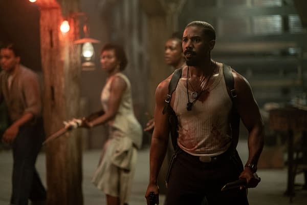 A tense scene from the movie 'Sinners', featuring a muscular man in a blood-stained sleeveless shirt holding a weapon, with two others in the background prepared for confrontation, illuminated by dim lighting.