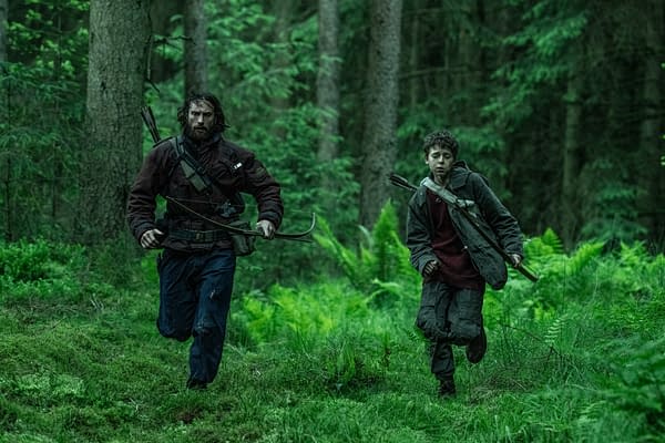 A scene depicting two characters running through a dense, green forest. The first character is an adult male, dressed in dark clothing and carrying a bow, while the second character is a young boy, also in dark clothing, appearing distressed as they navigate the wilderness.