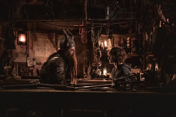 A scene from 'How To Train Your Dragon' featuring a bearded character in armor speaking to a young boy in a dimly lit workshop filled with various tools and decorations.