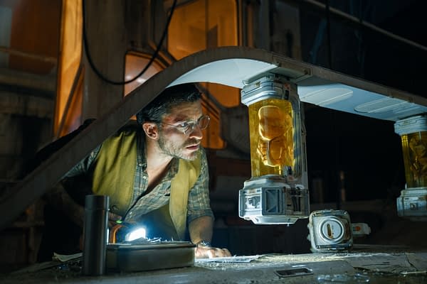 A scene from 'Jurassic World Rebirth' featuring Jonathan Bailey as Dr. Henry Loomis, intensely examining a yellow container holding a dinosaur embryo under a dim light, in a lab-like environment.